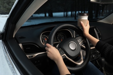 Photo of Young woman with coffee driving car along winter forest, closeup