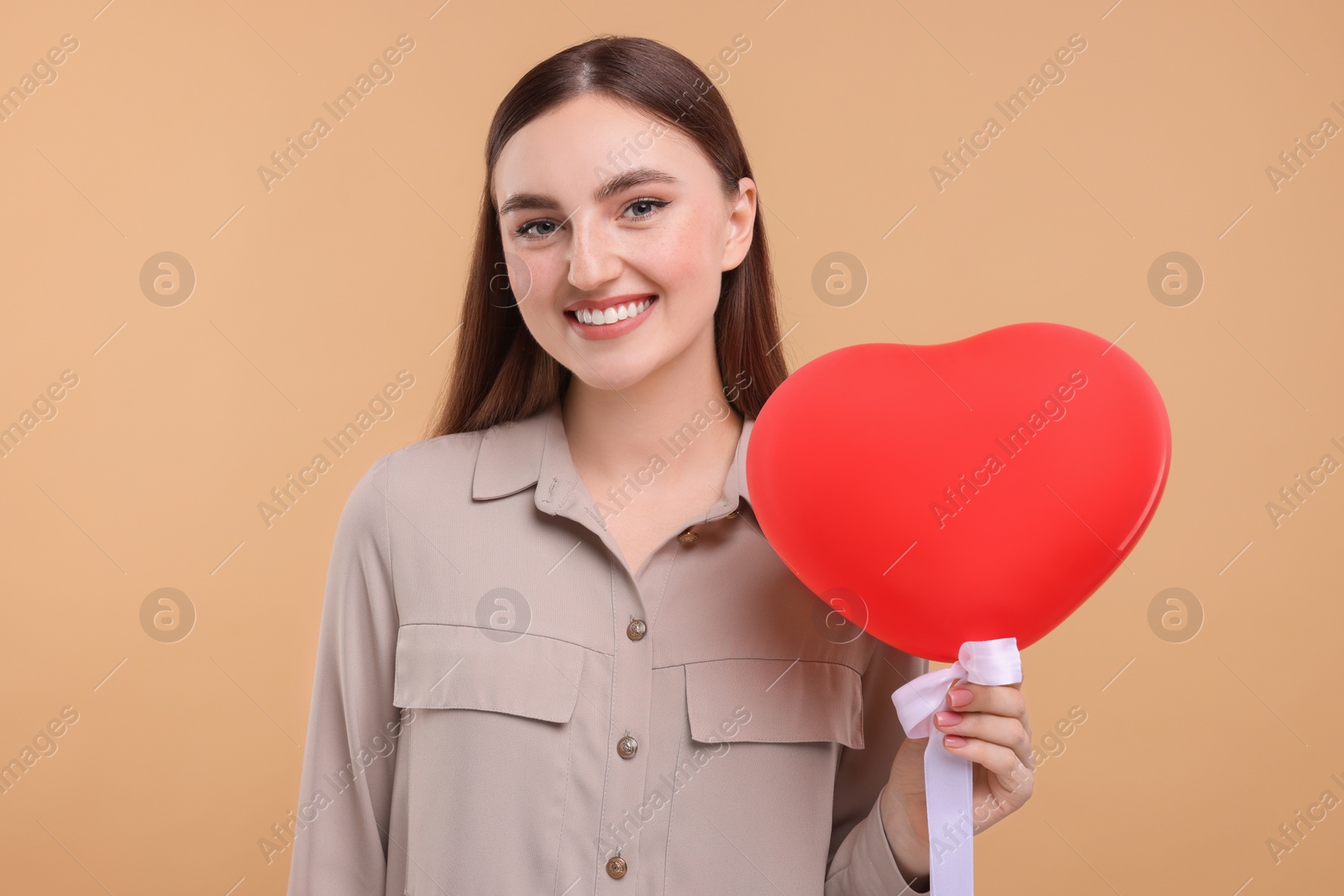 Photo of Smiling woman holding red heart shaped balloon on beige background