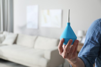 Man holding blue enema at home, closeup. Space for text