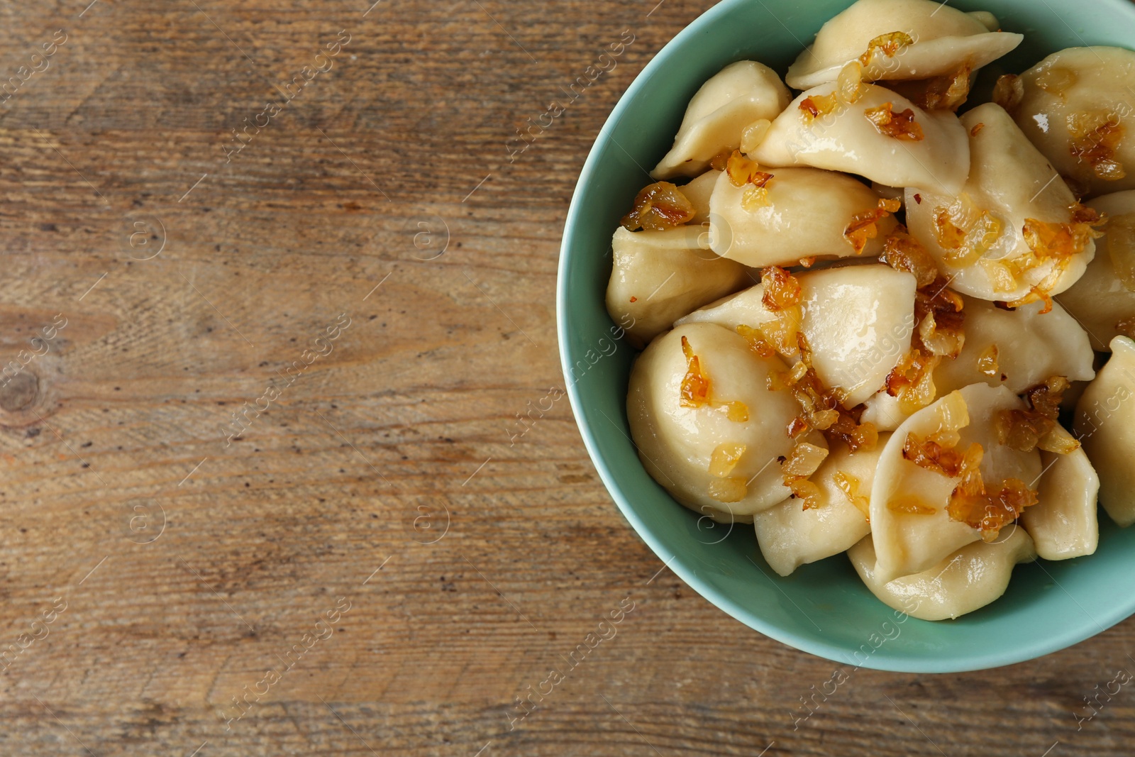 Photo of Delicious cooked dumplings with fried onion on wooden table, top view. Space for text