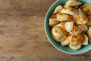 Photo of Delicious cooked dumplings with fried onion on wooden table, top view. Space for text