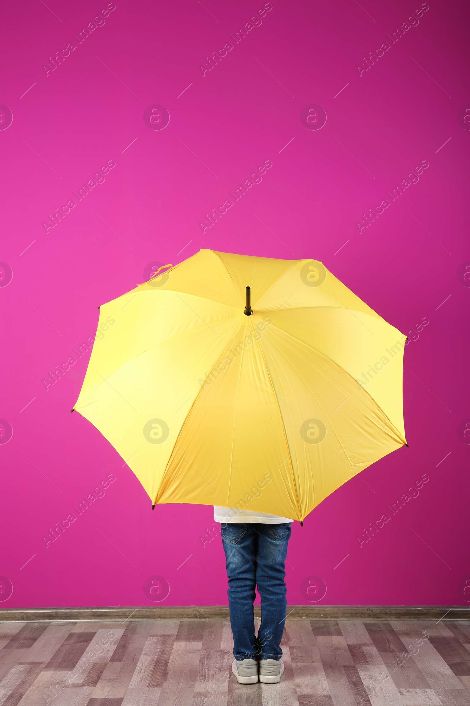 Photo of Little boy with yellow umbrella near color wall