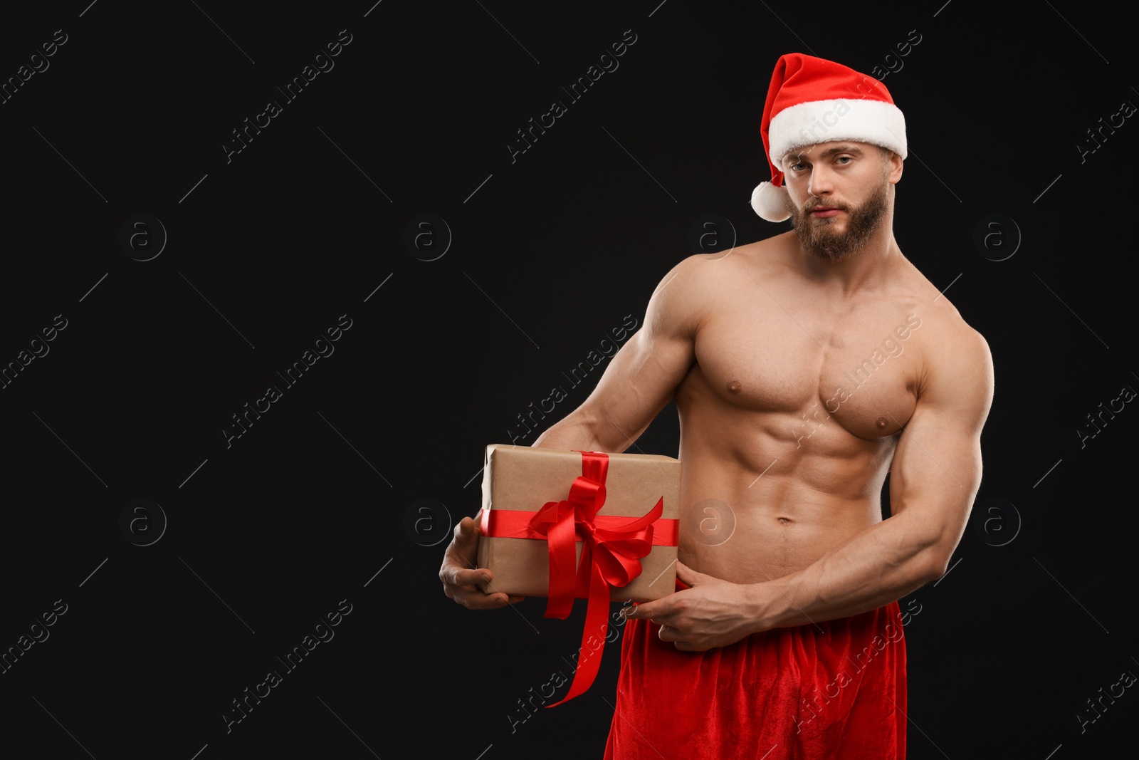 Photo of Attractive young man with muscular body holding Christmas gift box on black background, space for text