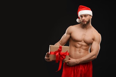 Photo of Attractive young man with muscular body holding Christmas gift box on black background, space for text