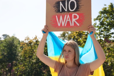 Sad woman holding poster with words No War and Ukrainian flag outdoors