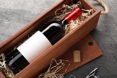 Bottle of wine in wooden box, cork and corkscrew on dark textured table, above view
