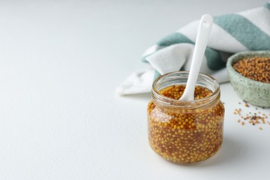 Whole grain mustard and spoon in jar on white table. Space for text
