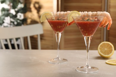 Photo of Tasty shrimp cocktail with sauce in glasses and lemon on light marble table, space for text