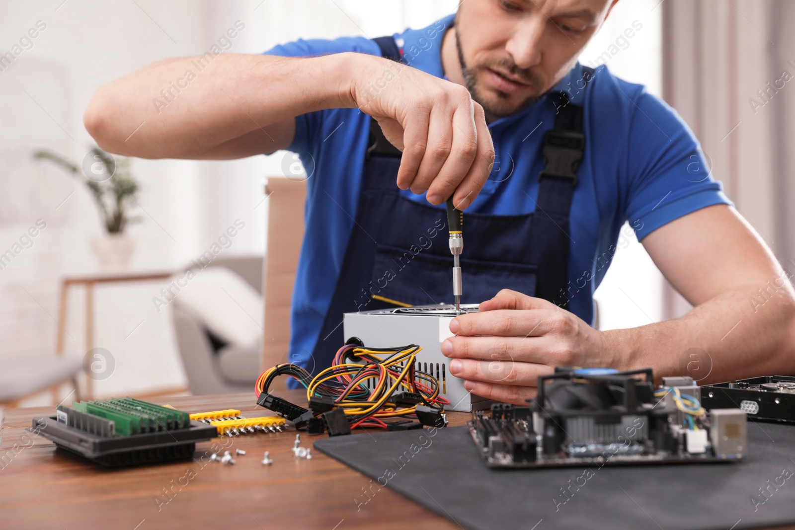 Photo of Male technician repairing power supply unit at table indoors