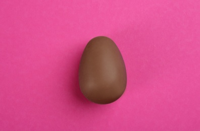 Sweet chocolate egg on pink background, top view