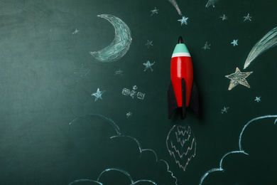 Photo of Bright toy rocket and drawings on chalkboard, top view. Space for text