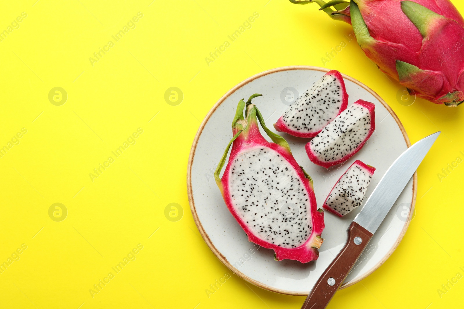 Photo of Plate with delicious cut white pitahaya fruit and knife on yellow background, flat lay. Space for text