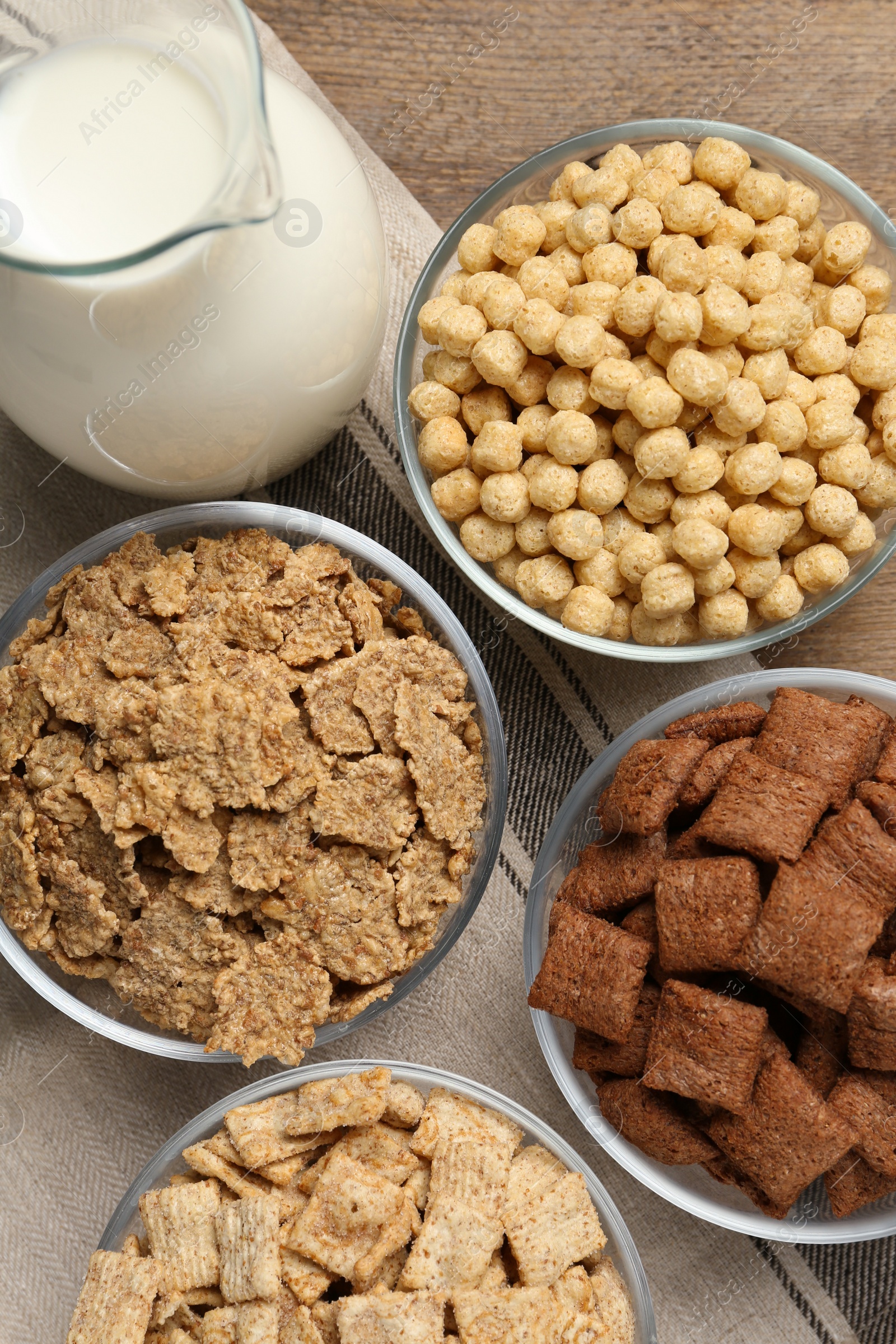 Photo of Different breakfast cereals and milk on wooden table, flat lay