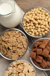Photo of Different breakfast cereals and milk on wooden table, flat lay
