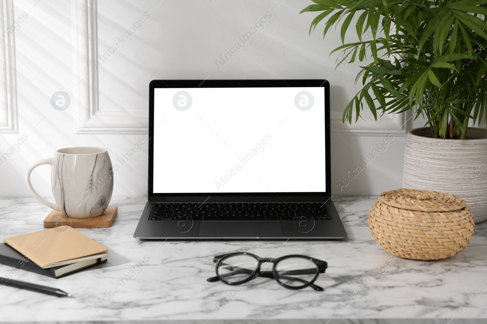 Photo of Office workplace with computer, glasses, cup and stationery on marble table near white wall