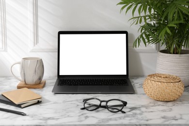 Photo of Office workplace with computer, glasses, cup and stationery on marble table near white wall