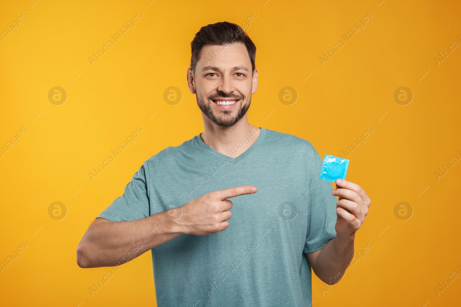 Photo of Happy man holding condom on orange background