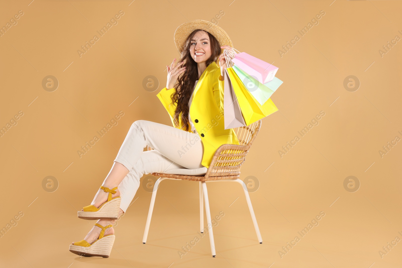 Photo of Happy woman holding many colorful shopping bags on armchair against beige background