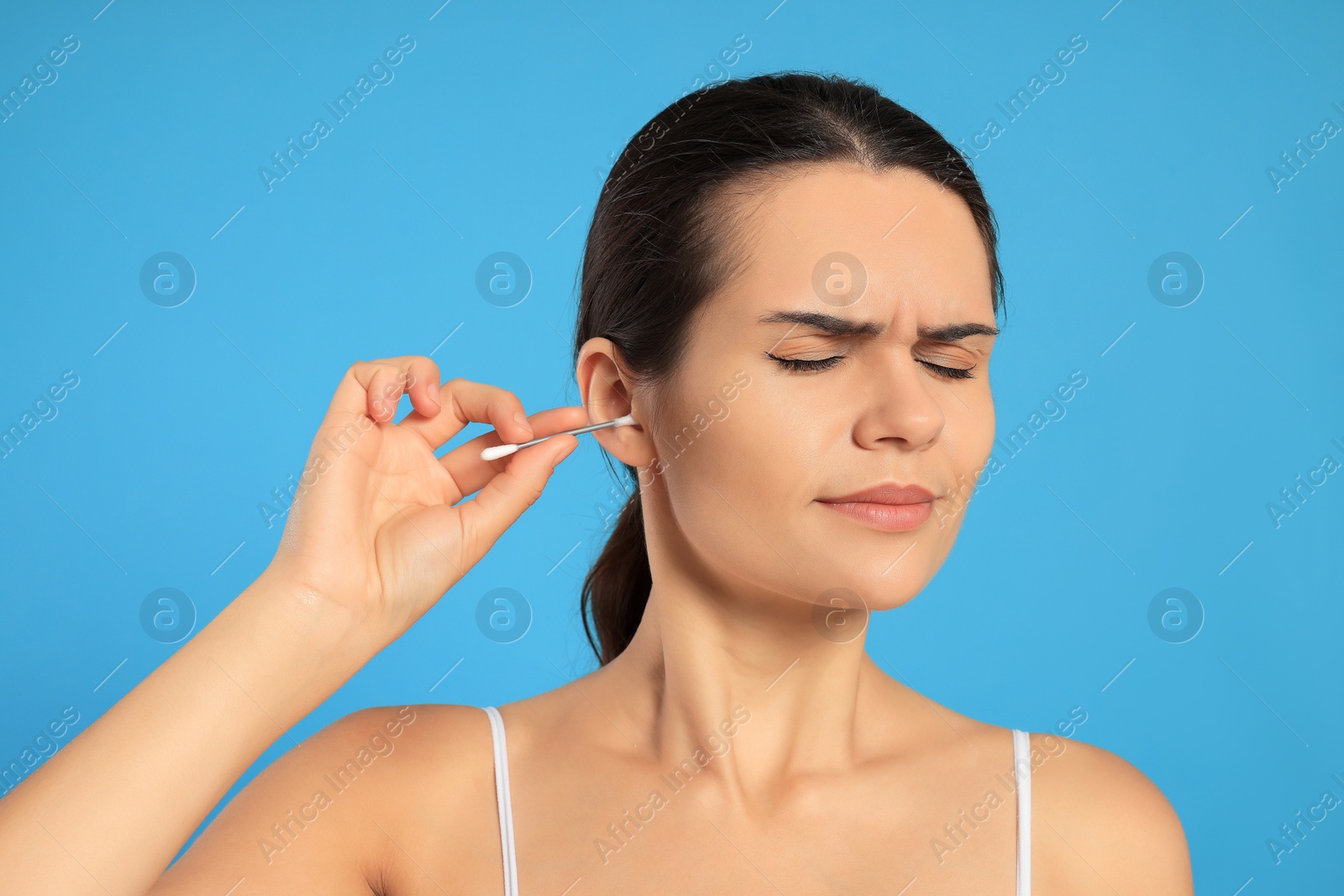 Photo of Young woman cleaning ear with cotton swab on light blue background