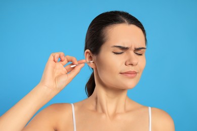 Photo of Young woman cleaning ear with cotton swab on light blue background