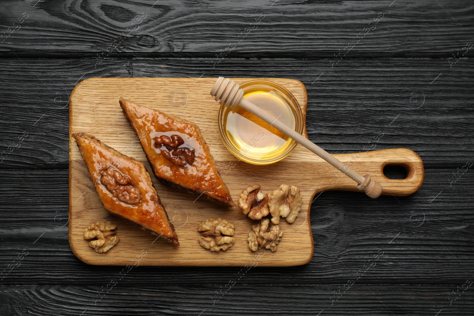 Photo of Delicious sweet baklava with walnuts and honey on black wooden table, top view