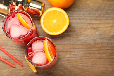 Tasty cranberry cocktail with ice cubes and orange in glasses on wooden table, flat lay. Space for text