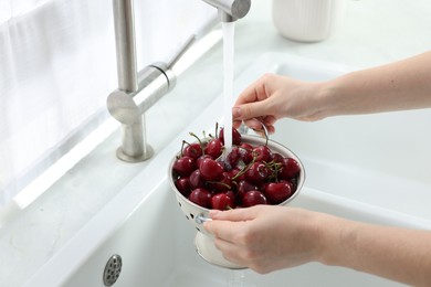Woman washing fresh ripe cherries under tap water in kitchen, closeup