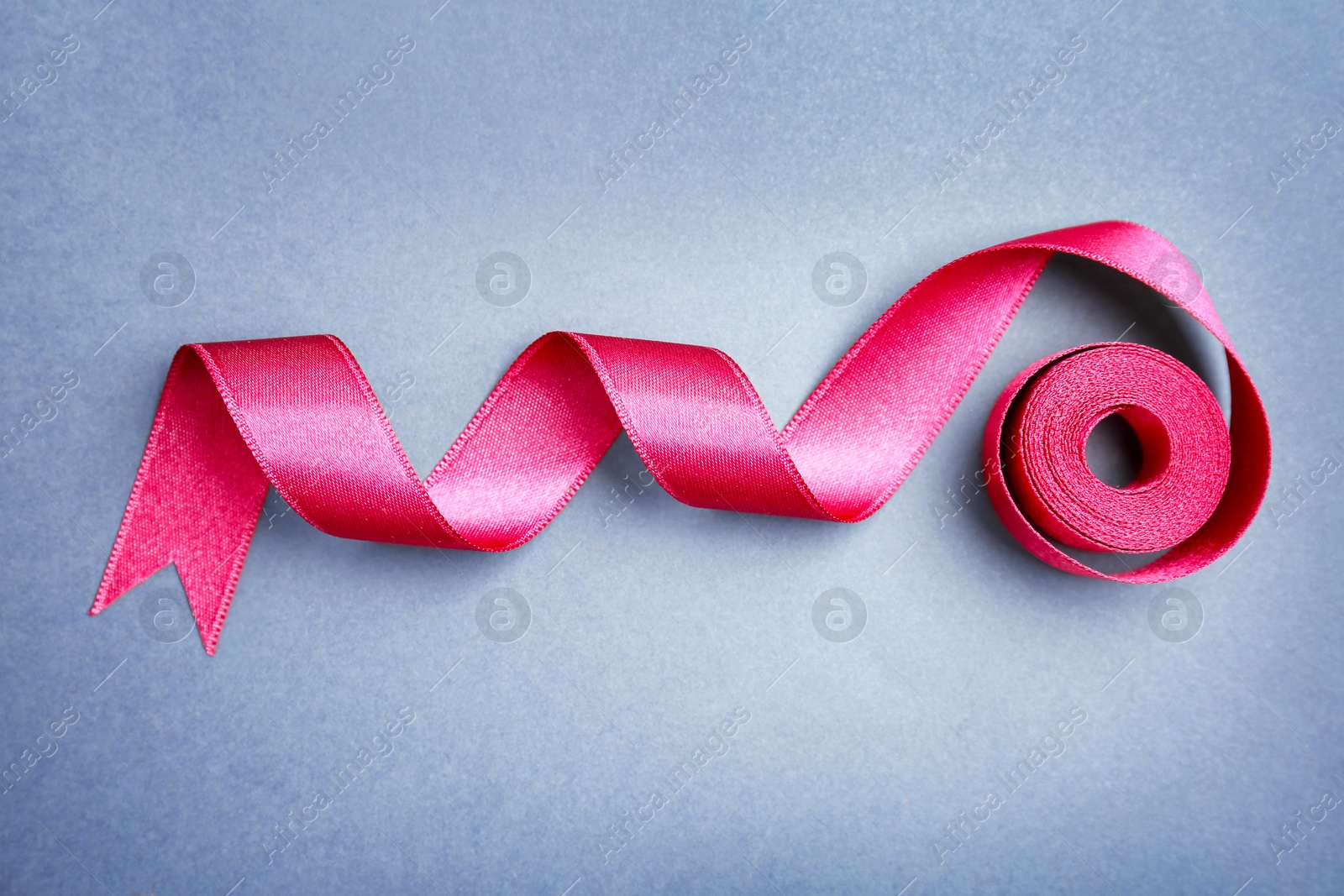 Photo of Simple pink ribbon on color background, top view