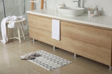 Photo of Soft bath mat and slippers on floor in bathroom