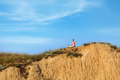Photo of Distant view of woman meditating on sandy hill