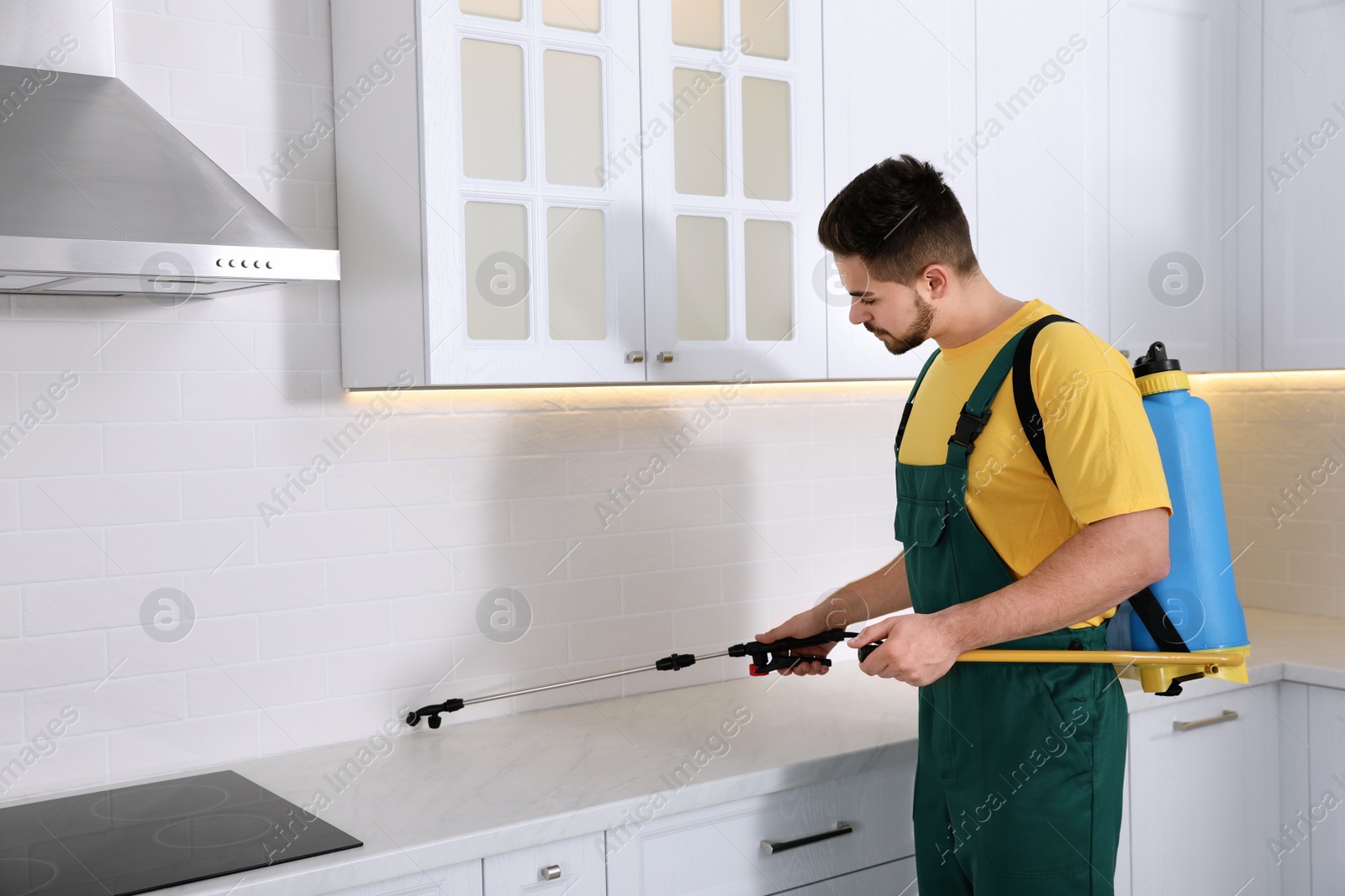 Photo of Pest control worker spraying insecticide on furniture in kitchen