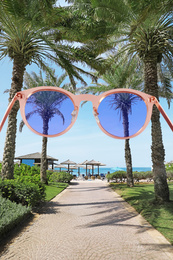 Palm alley leading to tropical beach on sunny day, view through sunglasses