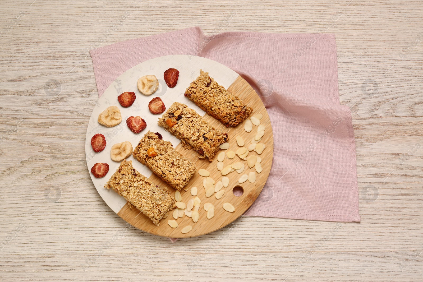 Photo of Tasty granola bars, dried strawberries, bananas and almond flakes on wooden table, top view