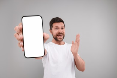 Surprised man showing smartphone in hand on light grey background