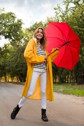 Beautiful young woman wearing stylish autumn clothes with red umbrella in park