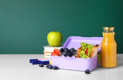 Photo of Lunch box with healthy food and different stationery on white wooden table near green chalkboard, space for text