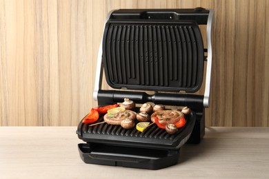 Photo of Electric grill with homemade sausages, mushrooms and bell pepper on wooden table