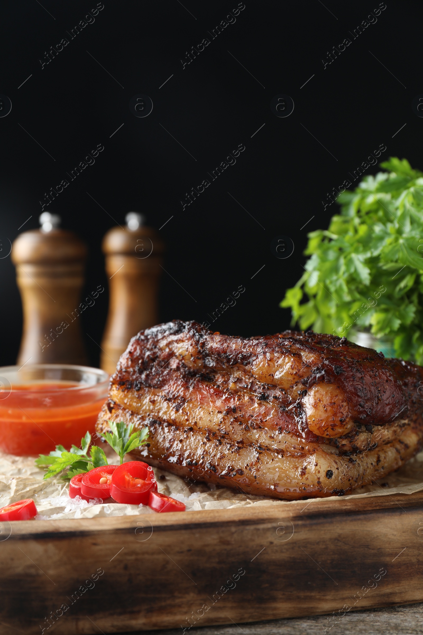 Photo of Piece of baked pork belly served with sauce and chili pepper on wooden table