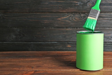 Paint can and dipped brush on table against wooden background. Space for text