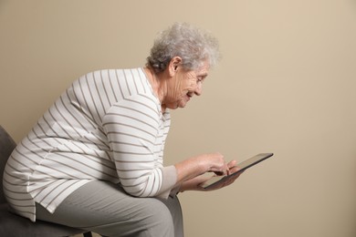 Elderly woman with poor posture using tablet on beige background