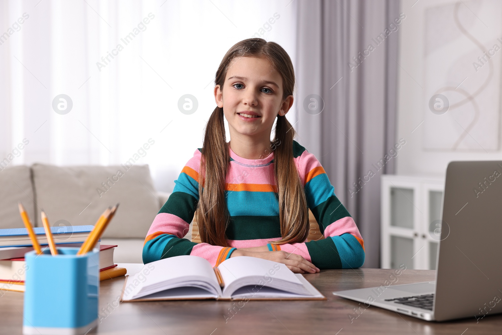 Photo of E-learning. Cute girl using laptop during online lesson at table indoors