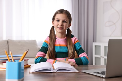 Photo of E-learning. Cute girl using laptop during online lesson at table indoors