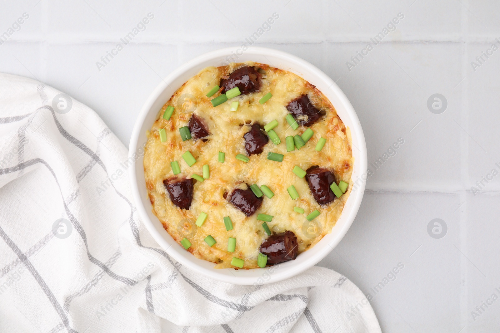 Photo of Tasty sausage casserole with green onions in baking dish on white tiled table, top view