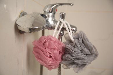Photo of Colorful shower puffs hanging on faucet in bathroom, closeup