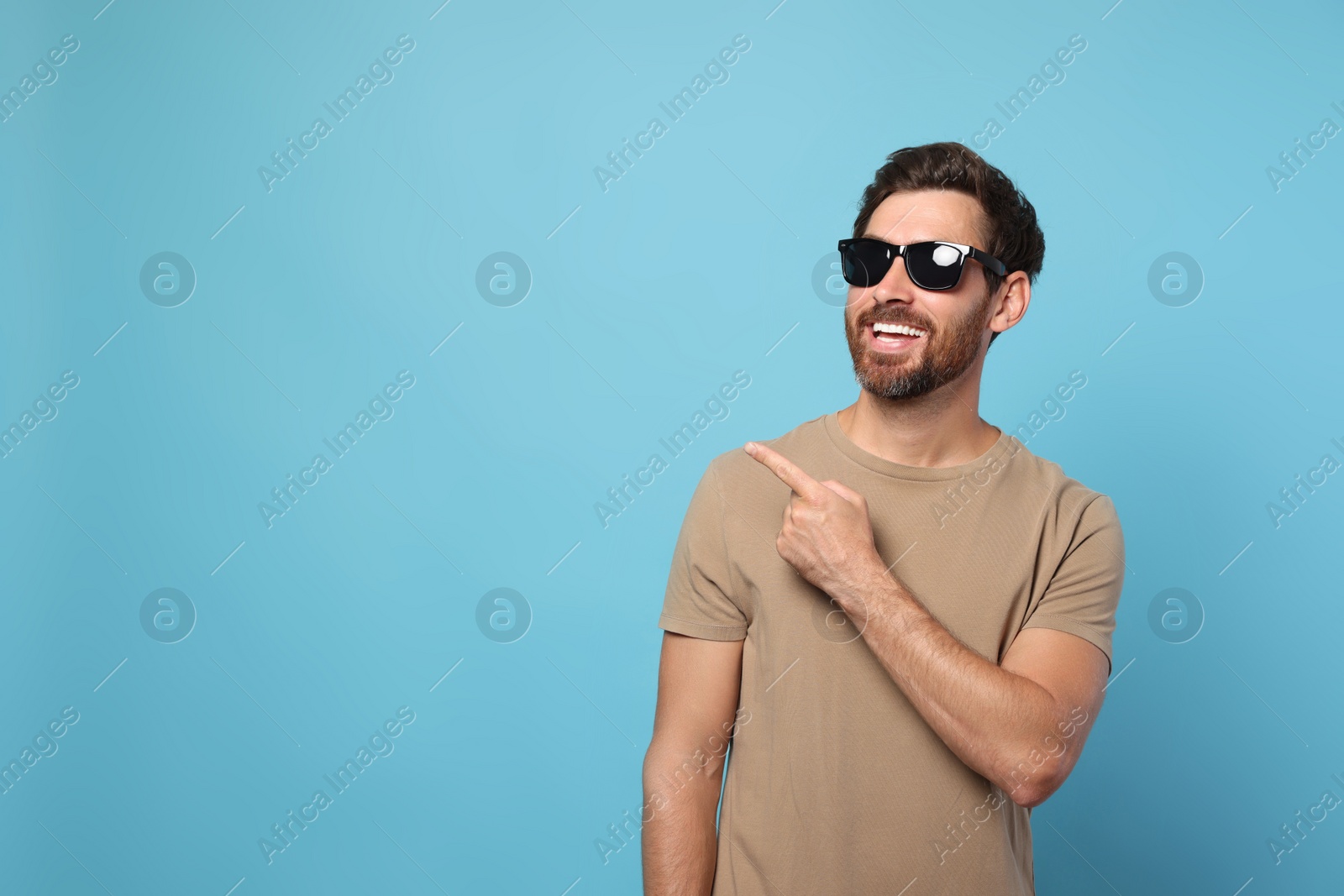 Photo of Portrait of smiling bearded man with stylish sunglasses on light blue background. Space for text