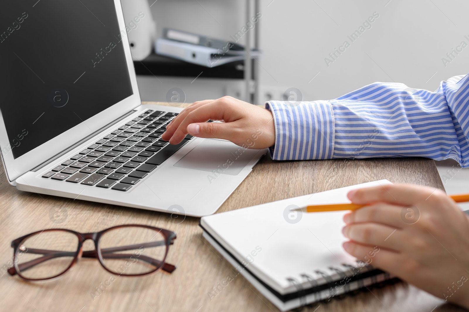 Photo of Woman with notebook working on laptop at wooden table in office, closeup