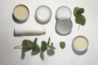 Different lip balms and leaves on white textured background, flat lay