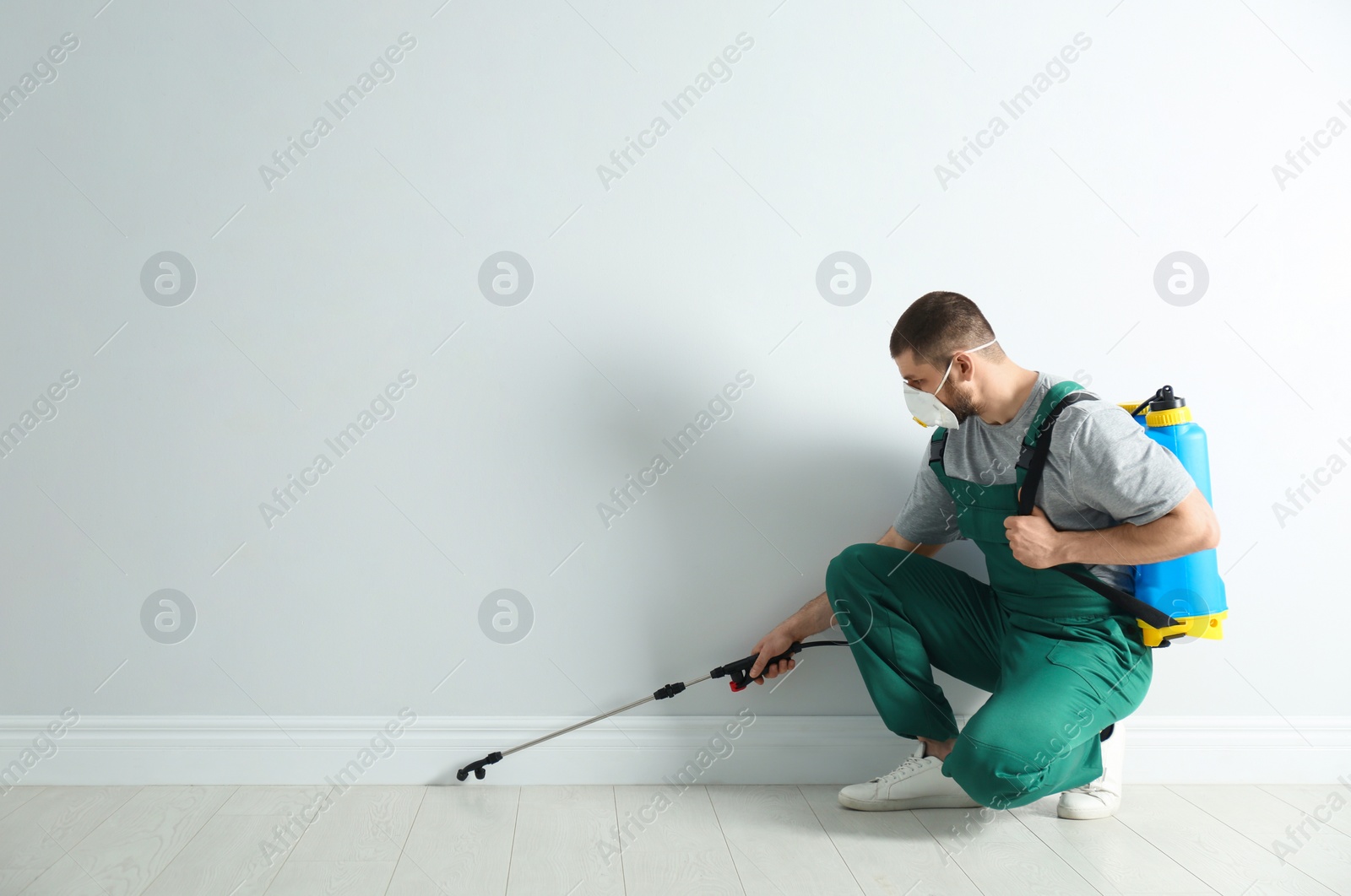 Photo of Pest control worker in uniform spraying pesticide indoors. Space for text