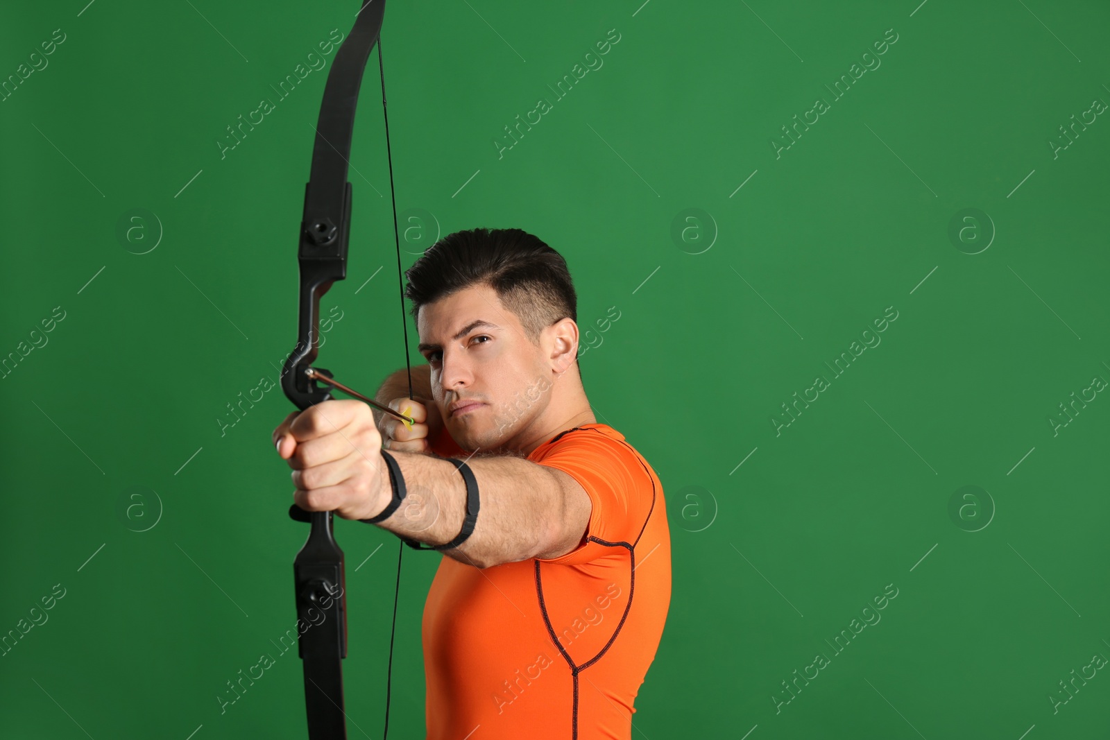 Photo of Man with bow and arrow practicing archery on green background, space for text