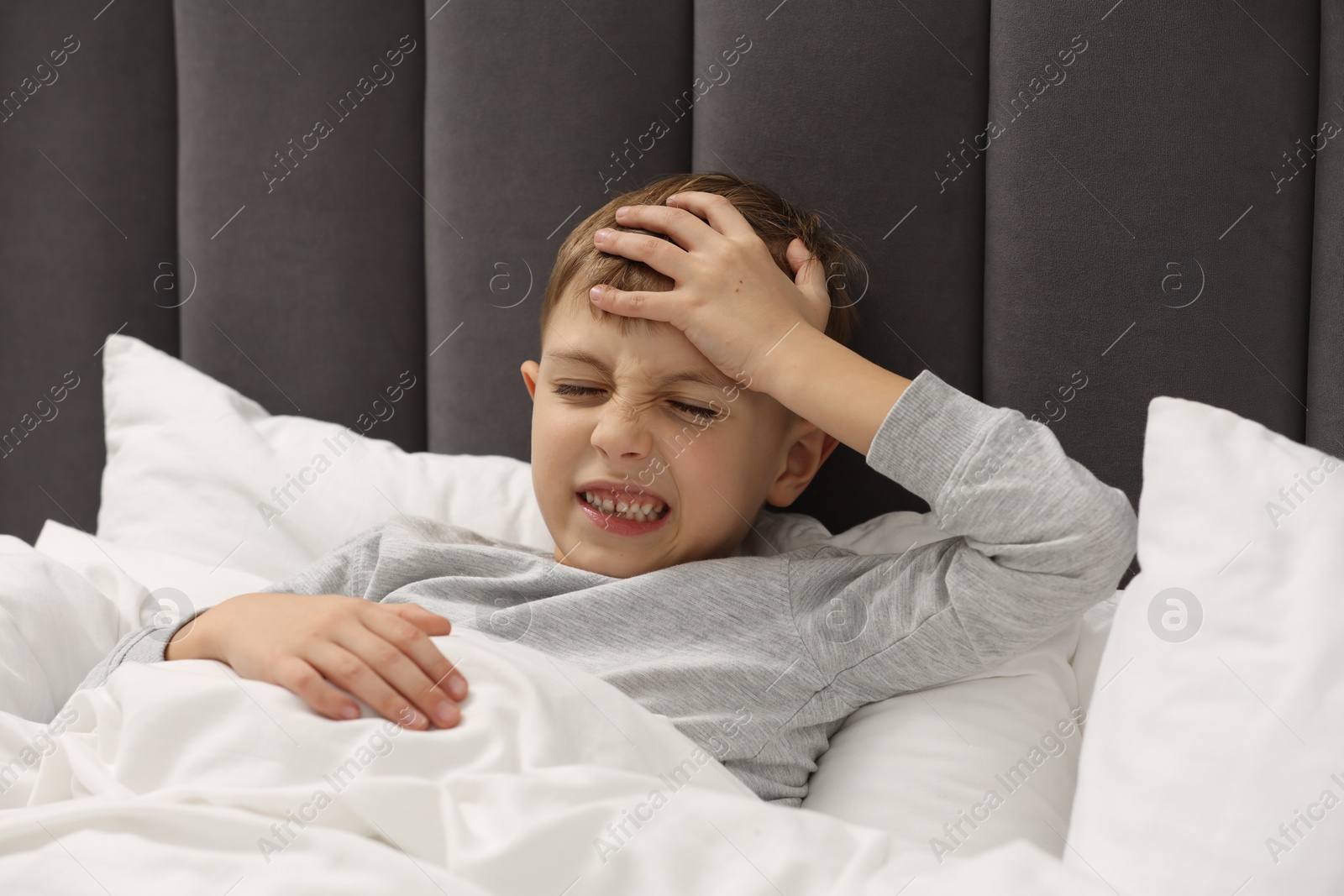 Photo of Little boy suffering from headache in bed at home